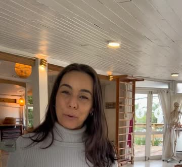 Fernanda na sala durante o dia, com a espaldar de madeira e as janelas ao fundo